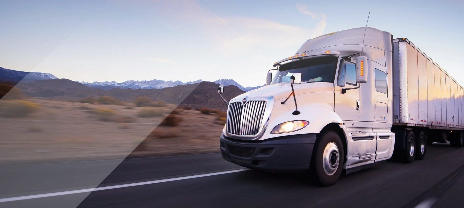 A white truck driving down the road near some mountains.